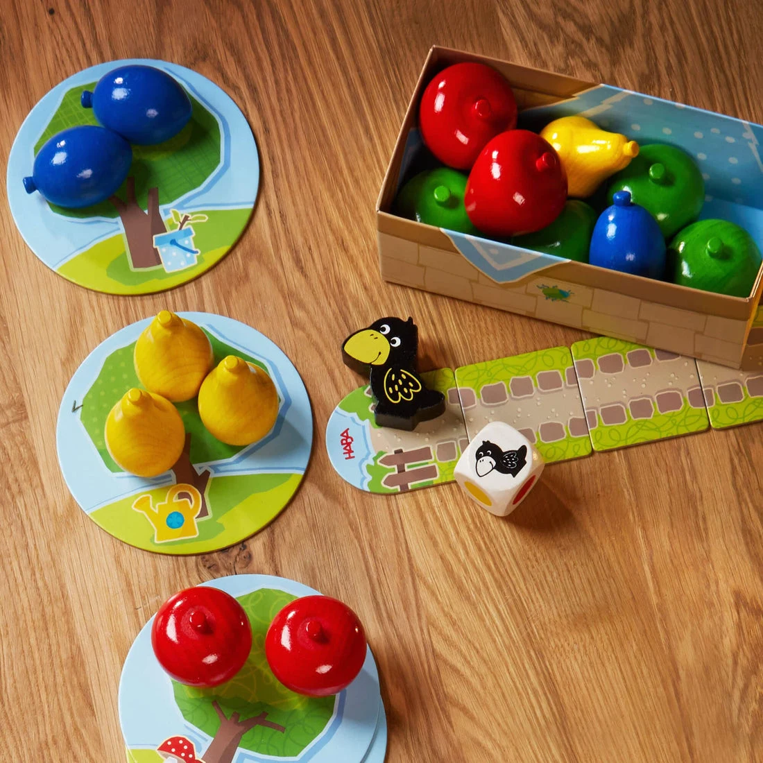 Colorful wooden fruit and a raven arranged for a game of HABA First Orchard